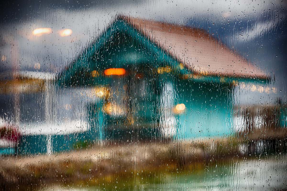 le bistrot du port window glass filled with water drops and a view of teal wooden house sévrier